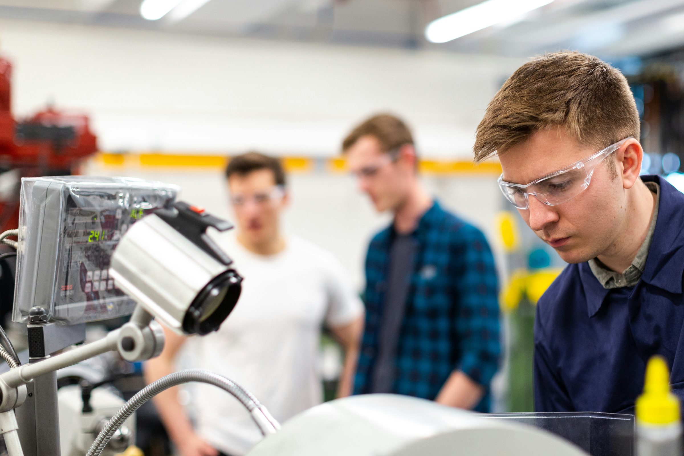 An engineer in safety glasses checking a part on a machine